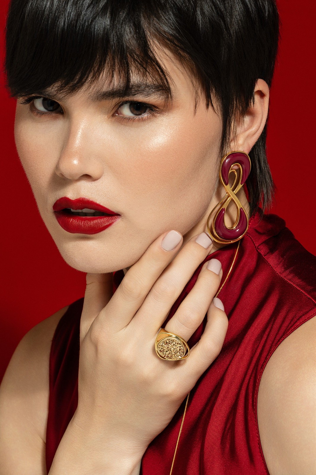 Retrato de modelo com anéis e brincos dourados sobre fundo vermelho